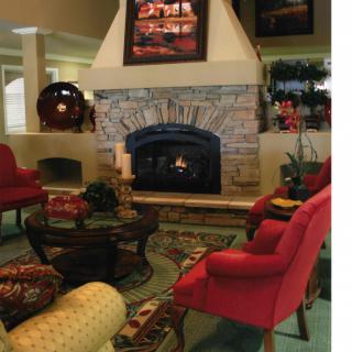 A cozy living room with a stone fireplace surrounded by red chairs and warm decor.