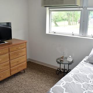A cozy bedroom with a dresser, TV, and side table next to the bed.