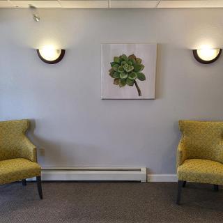 A minimalist waiting room with two yellow chairs and artwork on the wall.