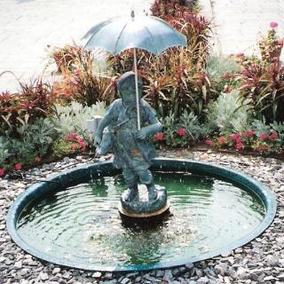 A garden fountain featuring a statue holding an umbrella surrounded by plants.