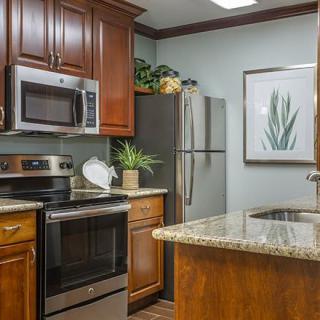 A modern kitchen featuring stainless steel appliances, wood cabinets, and a granite countertop.