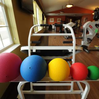 A variety of colorful exercise balls arranged on a rack in a gym setting.