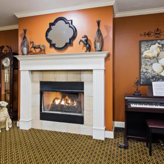 A cozy living room with a fireplace and a piano, featuring warm decor and artwork.