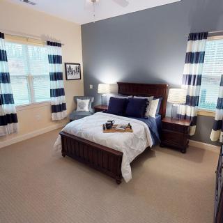 A cozy bedroom with a well-made bed, two windows with patterned curtains, and matching bedside lamps.