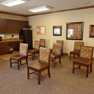 An empty meeting room with arranged chairs and kitchen area in the background.