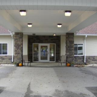 A building entrance with stone pillars and a covered entryway, featuring double doors and outdoor lighting.