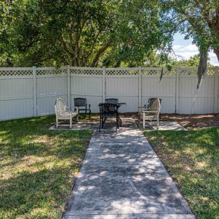 A backyard patio area with chairs and a table, surrounded by a white fence.