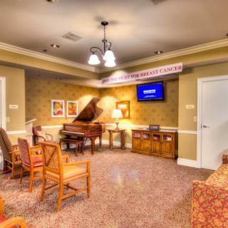 A cozy room with a grand piano, comfortable seating, and a television on the wall.