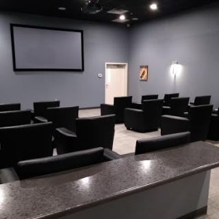 A cozy modern theater room with comfortable black seating and a large screen.