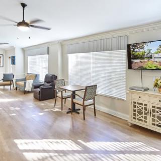 A modern living room with abundant natural light, featuring comfortable seating, a ceiling fan, and a wall-mounted TV.