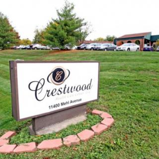 A sign for Crestwood placed on a grassy area with a building and parked cars in the background.