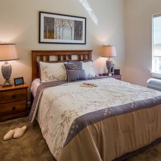 A cozy and well-decorated bedroom with a neatly made bed, bedside lamps, and framed artwork above the headboard.