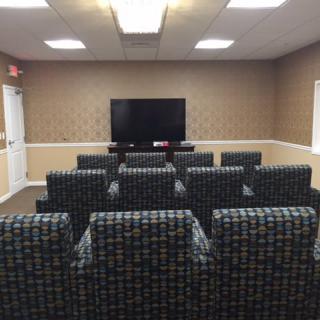 A small home theater room with multiple rows of comfortable seating facing a large television screen.