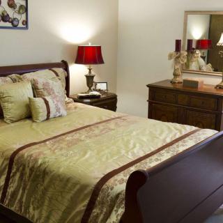 A cozy bedroom featuring a neatly made bed with decorative pillows, a wooden dresser, and a warmly lit lamp.