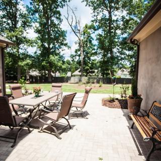 A sunny patio with outdoor furniture surrounded by a lush backyard.
