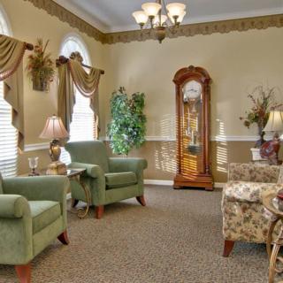 A cozy living room with classic decor, featuring armchairs, a grandfather clock, and elegant curtains.