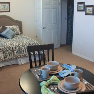 A cozy bedroom with an adjacent dining area, featuring a neatly set table and comfortable bedding.