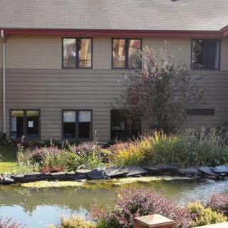 A two-story building with large windows, surrounded by a landscaped garden and pond.