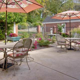 A peaceful outdoor patio with tables, chairs, and umbrellas surrounded by a garden.