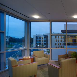 A cozy lobby area with comfortable chairs and large windows overlooking a modern building at dusk.