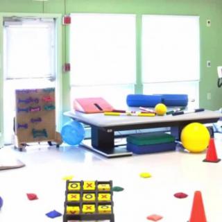 A brightly lit physical therapy room equipped with exercise materials and colorful objects.