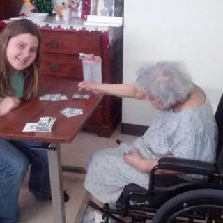 A young girl and an elderly woman in a wheelchair playing cards together indoors.