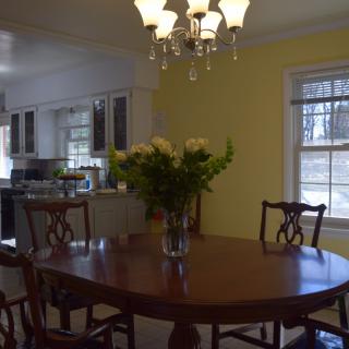 A cozy dining area with a round table and a vase of flowers, adjacent to a kitchen.