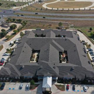 Aerial view of a large building with parking lots and a nearby highway.