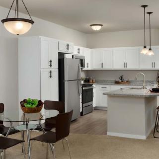 A modern kitchen with white cabinets, a center island, and stainless steel appliances, adjacent to a small dining area with a glass table.