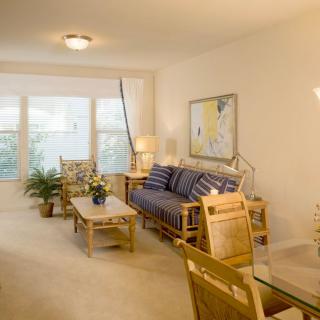 A cozy living room with rattan furniture, a blue-striped sofa, and large windows providing natural light.