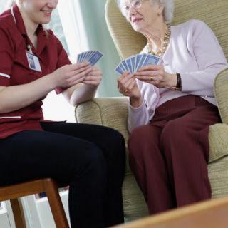 A caregiver playing cards with an elderly woman in a comfortable setting.