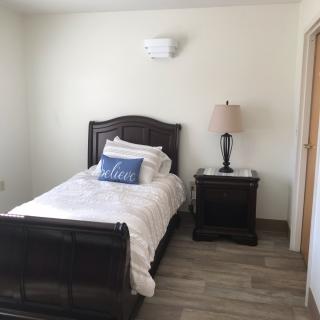 A simple bedroom with a single bed, nightstand, and lamp.