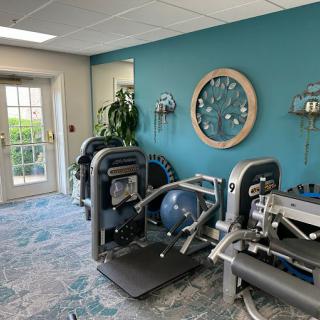 A small gym room with various exercise machines and a large wall clock.
