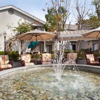 A serene outdoor patio featuring a central fountain, surrounded by chairs and umbrellas.