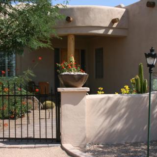 A southwestern-style adobe house with a gated entrance and a desert garden featuring cacti.
