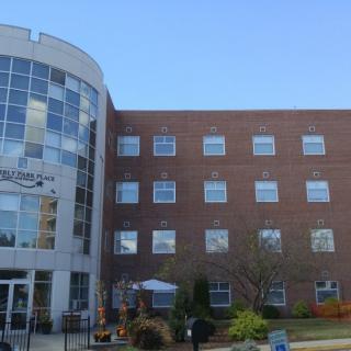 A modern brick building with large windows and a curved entrance, surrounded by greenery.