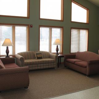 A cozy living room with sofas and lamps near large windows.