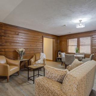 A cozy living room with wood paneling, featuring a sofa, chairs, and tables.
