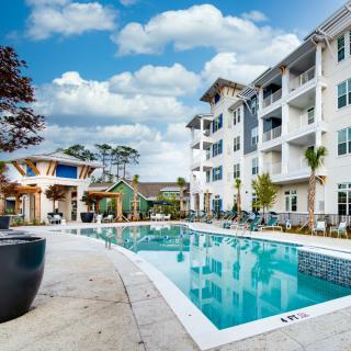 A modern apartment complex featuring an outdoor swimming pool under a partly cloudy sky.