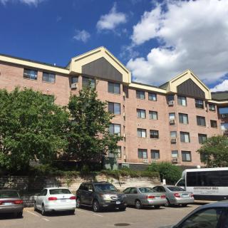 A view of a multi-story apartment building with a parking lot full of cars under a partly cloudy sky.