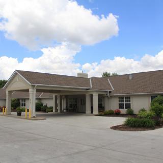 A one-story building with a covered entrance and driveway, set against a backdrop of clouds and blue sky.