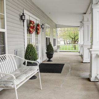A cozy porch with a white bench, decorative plants, and festive wreaths.