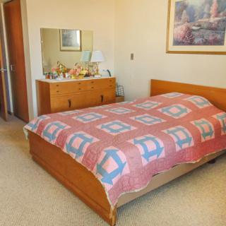 A cozy bedroom with a wooden bed adorned with a quilt, a dresser with a mirror, and framed artwork on the wall.
