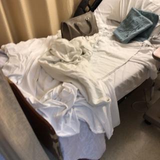 An unmade hospital bed with rumpled sheets and pillows.