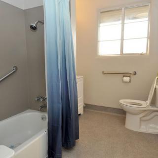 A spacious bathroom featuring a bathtub with a gradient shower curtain, a toilet, and handrails for accessibility.