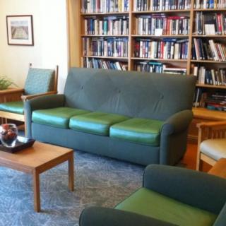 A cozy library area with a green sofa, chairs, and bookshelves filled with books.