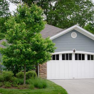 A suburban house with a two-car garage and a tree in the front yard.