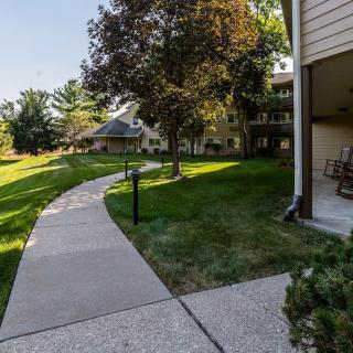 A sunny outdoor scene with a winding pathway, surrounded by grass and trees, next to residential buildings.