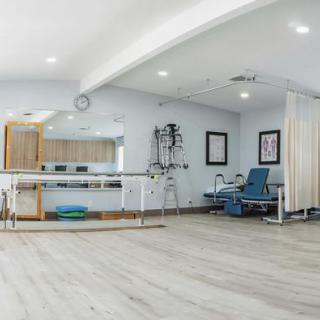 A spacious rehabilitation center equipped with physical therapy apparatus and seating.