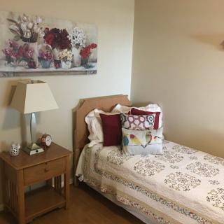 A cozy bedroom with a single bed, nightstand, and floral artwork.
